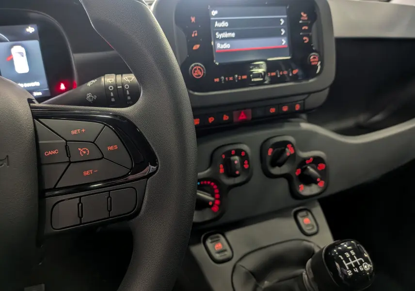 Intérieur de la Fiat Panda 2025 bleu Italia, vue rapprochée sur le volant, la console centrale et le levier de vitesses manuel.