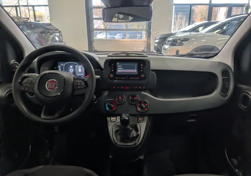 Vue intérieure avant du tableau de bord de la Fiat Panda 1.0 Hybrid 2025 avec volant, écran tactile et levier de vitesses manuel.