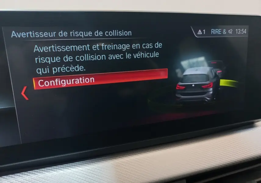 Écran tactile intérieur montrant l'alerte de risque de collision avec illustration d'un BMW X1 noir vue arrière.