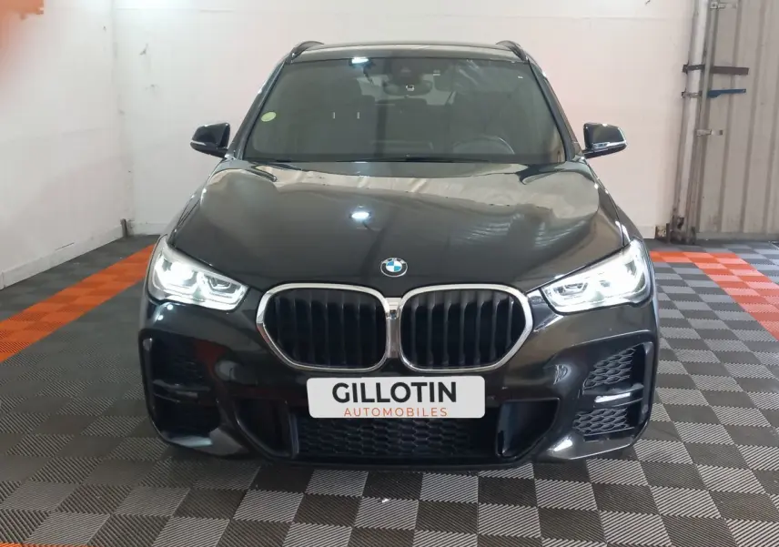 Vue avant d'un BMW X1 xDrive20d M Sport noir avec phares LED allumés dans un garage.