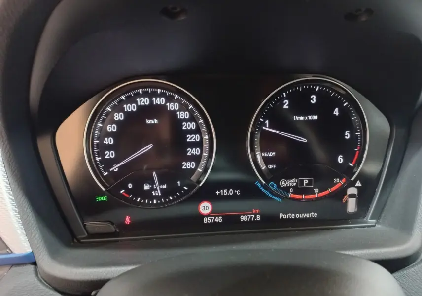 Gros plan sur le tableau de bord numérique du BMW X1 noir, affichant la vitesse, le régime moteur et les alertes.