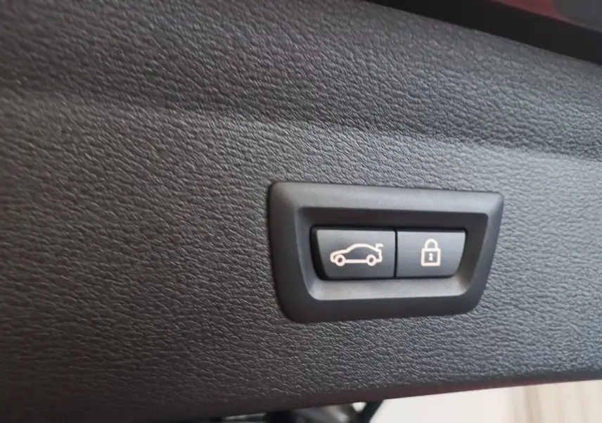 Gros plan sur les boutons d'ouverture et de verrouillage du coffre, intérieur noir du BMW X1 xDrive20d M Sport 2022.