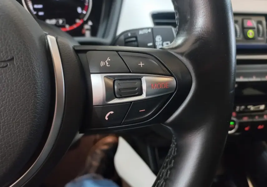 Gros plan sur les commandes du volant cuir noir de la BMW X1 xDrive20d M Sport, avec bouton mode rouge visible.