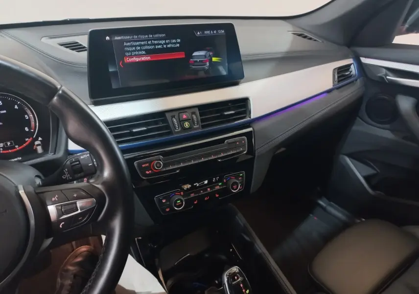 Vue intérieure côté conducteur du tableau de bord et écran tactile d'une BMW X1 noire, avec éclairage d'ambiance violet.