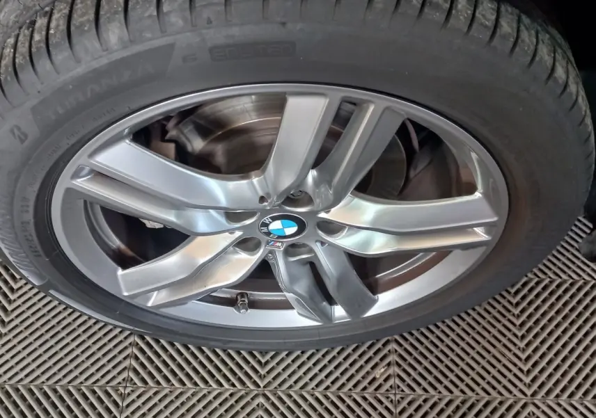 Gros plan sur la jante alliage argentée avec logo BMW et pneu Bridgestone d’un BMW X1 noir.