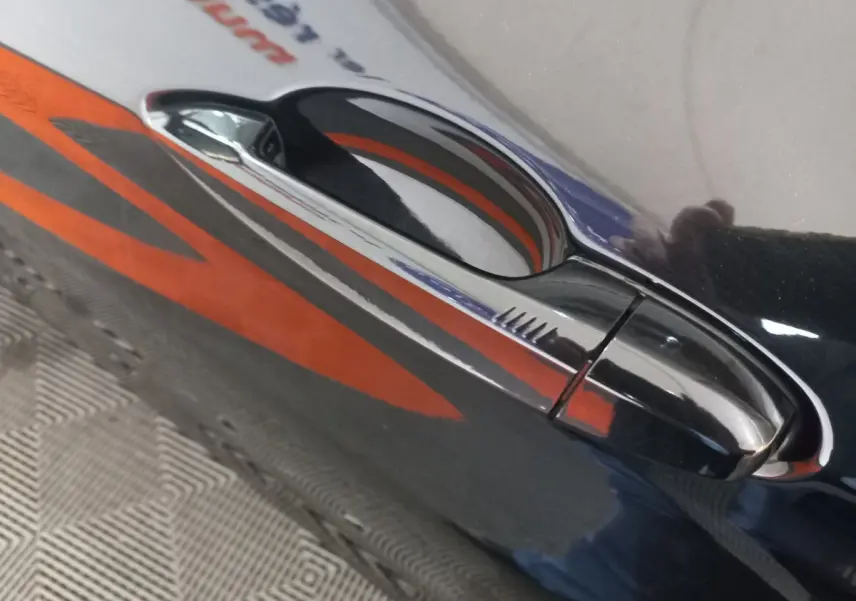 Poignée de porte noire brillante côté droit d’un BMW X1 xDrive20d M Sport 2022 avec reflet orange.