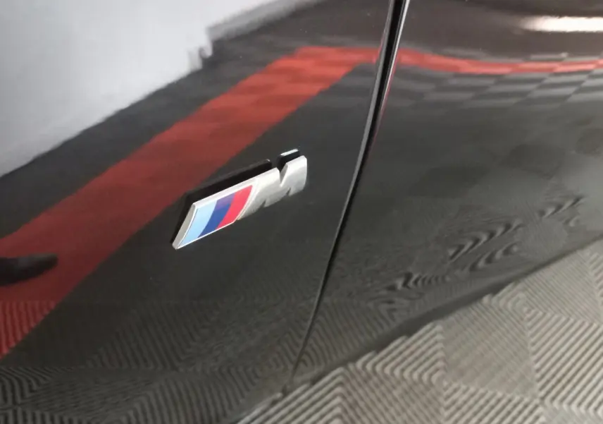 Gros plan sur l'emblème M sur la porte noire brillante d'une BMW X1 xDrive20d M Sport 2022.