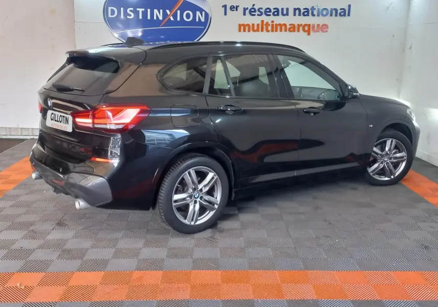 Vue 3/4 arrière droite d'un BMW X1 noir garé en intérieur avec jantes alliage et feux arrière allumés.