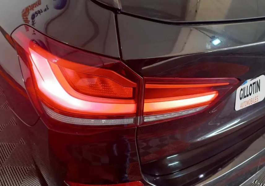 Gros plan sur le feu arrière droit allumé d’un BMW X1 xDrive20d M Sport noir, avec partie de la malle visible.