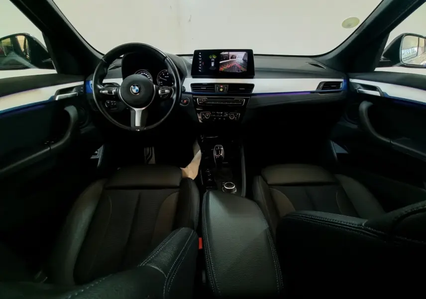 Vue intérieure avant du BMW X1 noir 2022, tableau de bord avec écran tactile et volant cuir multifonctions.