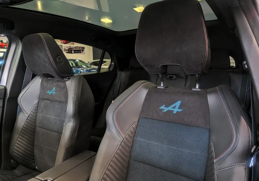 Gros plan sur les sièges avant en cuir noir et alcantara avec logo Alpine bleu, intérieur du Renault Rafale 2025.