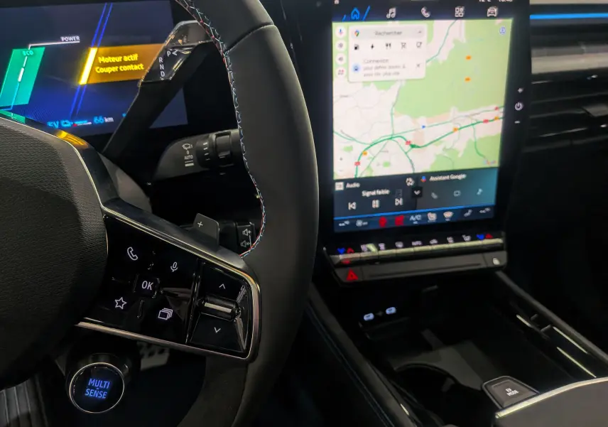 Vue intérieure rapprochée du volant avec commandes tactiles et écran central tactile affichant la navigation sur Renault Rafale hybride.