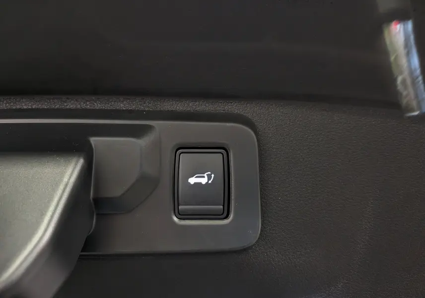 Gros plan sur le bouton d'ouverture du coffre intérieur du Renault Rafale gris Schiste Satin, version hybride rechargeable.