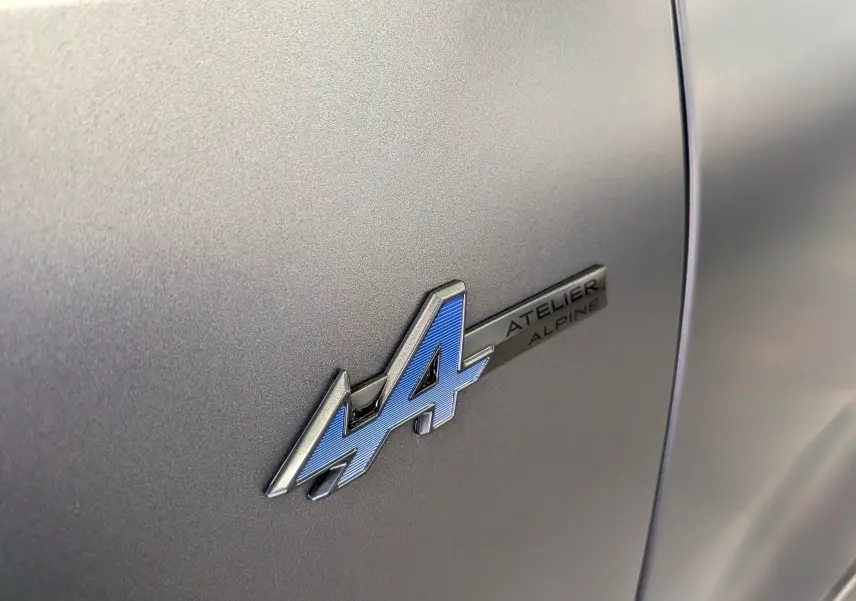 Gros plan sur l’insigne bleu et argent "4 Atelier Alpine" sur la carrosserie gris schiste satin du Renault Rafale.