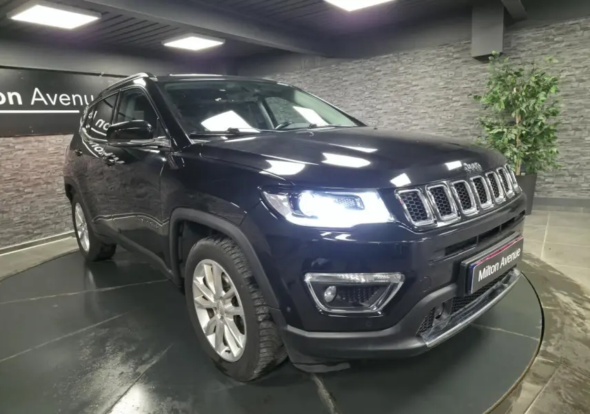 Jeep Compass noir en 3/4 avant droit avec phares allumés, jantes alliage 18 pouces et calandre chromée.