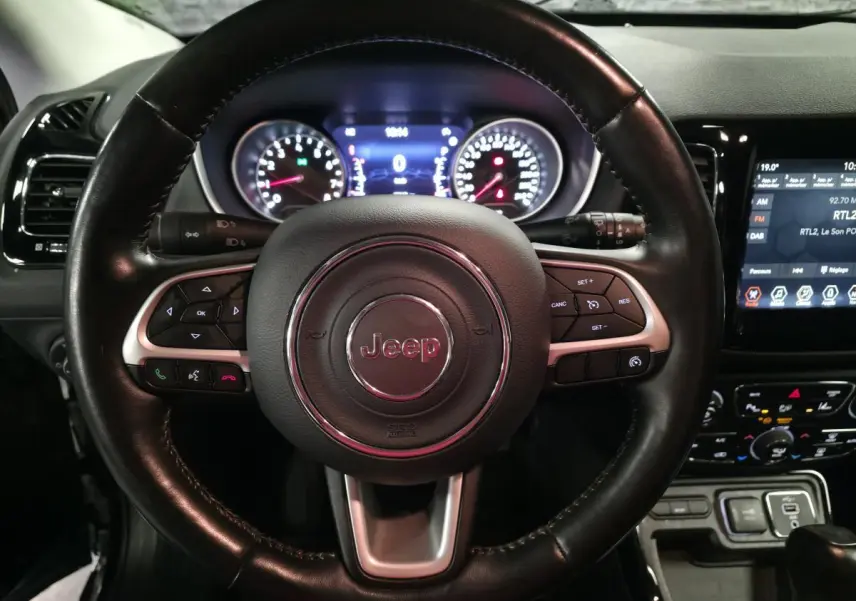 Vue rapprochée du volant cuir noir Jeep Compass 2021 avec commandes intégrées et tableau de bord numérique éclairé.