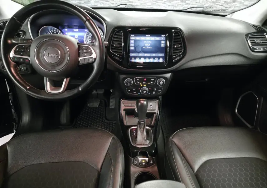 Vue intérieure avant du tableau de bord noir du Jeep Compass 2021 avec volant cuir et écran tactile central.
