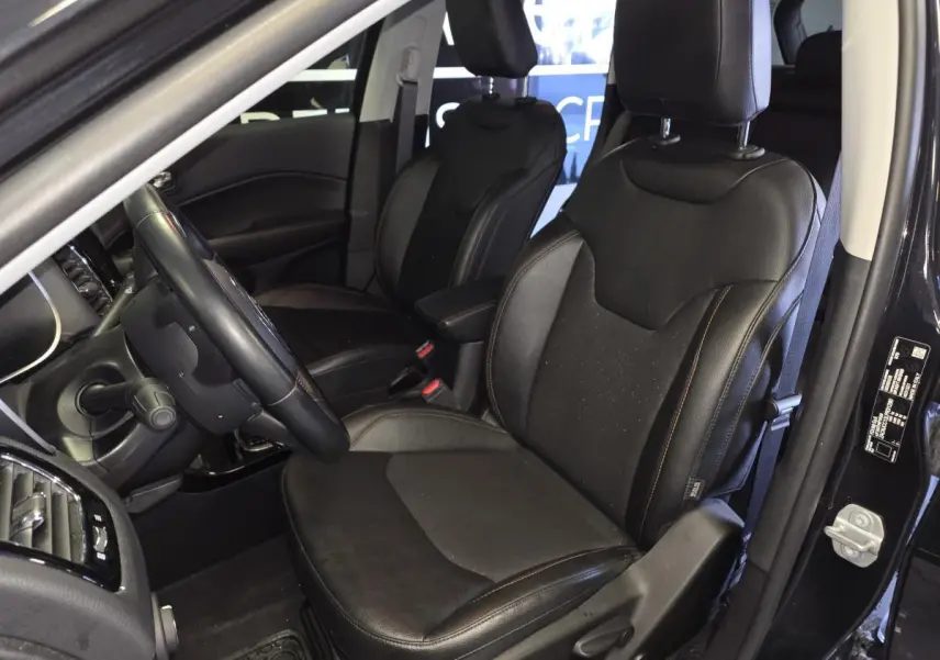 Vue intérieure côté conducteur du Jeep Compass 2021 noir, sièges simili cuir noirs avec volant cuir et console visible.
