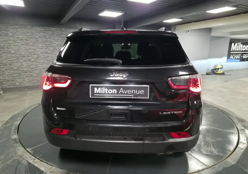 Vue arrière d'un Jeep Compass noir Limited 2021 avec feux arrière allumés dans un showroom.