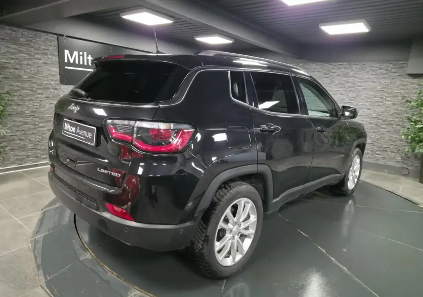Jeep Compass noir en 3/4 arrière droit, avec vitres surteintées et jantes alliage 18 pouces visibles en intérieur showroom.