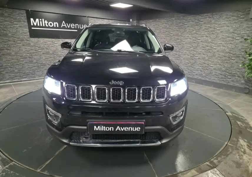 Vue frontale d'un Jeep Compass noir avec calandre chromée et phares LED allumés en intérieur showroom.