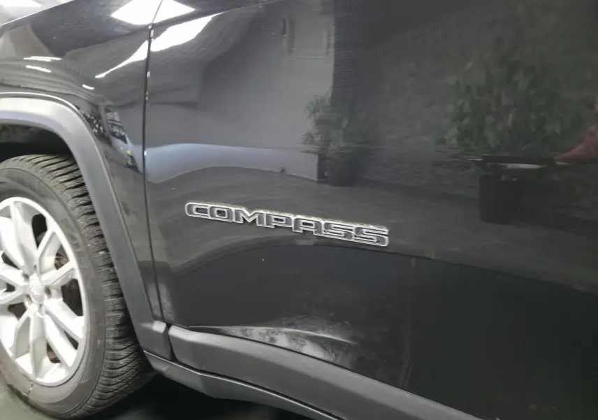 Gros plan sur le côté gauche noir brillant d’un Jeep Compass avec logo "COMPASS" près de la roue avant.
