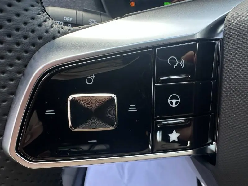 Gros plan sur les commandes noires et argentées au volant cuir du MG ZS Hybrid+ 197ch Comfort blanc, côté gauche.