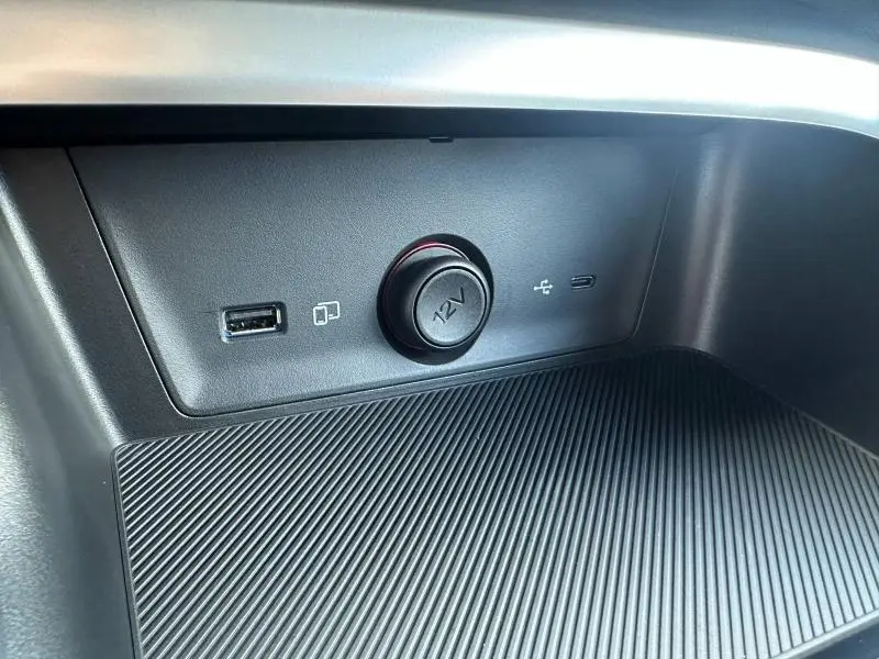Prise 12V et port USB intégrés dans la console centrale noire du MG ZS Hybrid+ 2025, détail intérieur.
