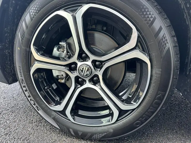 Gros plan sur la jante alu noire et argentée avec logo MG d’un MG ZS Hybrid+ blanc, vue côté roue avant.