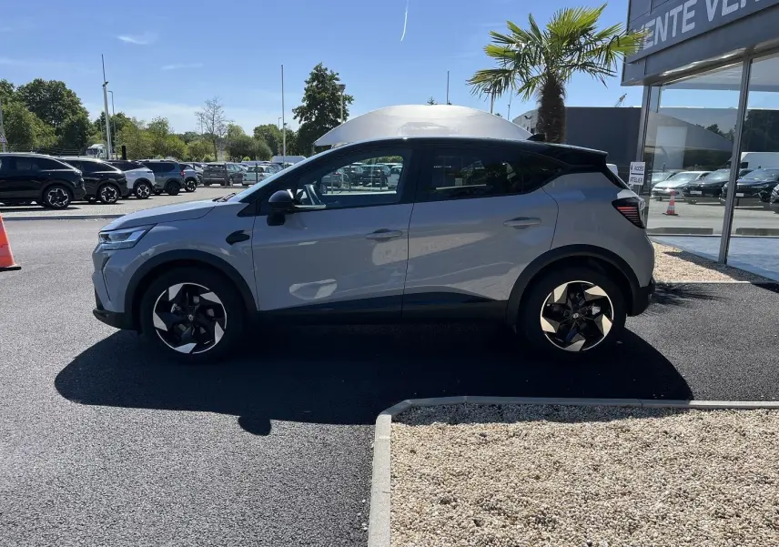 Profil côté gauche d'un Renault Captur gris Rafale avec toit noir, roues noires à jantes 18 pouces biton, stationné en extérieur.