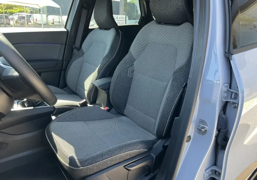 Vue intérieure côté conducteur du Renault Captur 2025, montrant les sièges tissu gris avec surpiqûres contrastantes.