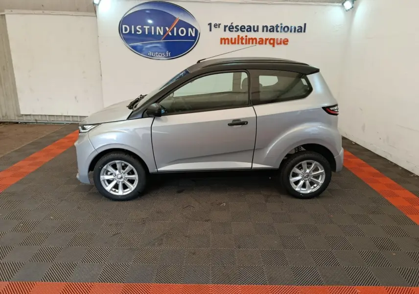 Vue de profil côté gauche d'une Aixam Ambition 0.5 City Crossline Pack gris foncé avec toit noir en intérieur showroom.