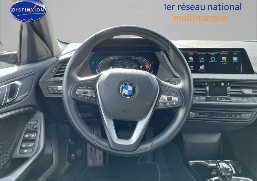 Vue frontale de l'intérieur de la BMW Série 1 118i 2021, volant cuir noir et tableau de bord digital lumineux.