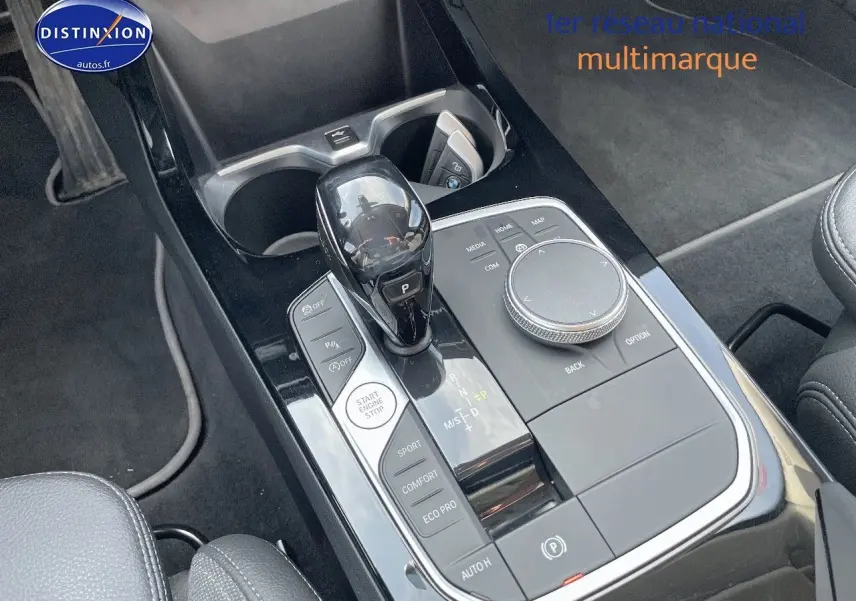 Gros plan sur la console centrale noire brillante de la BMW Série 1 gris minéral, avec levier de vitesse automatique et commandes.