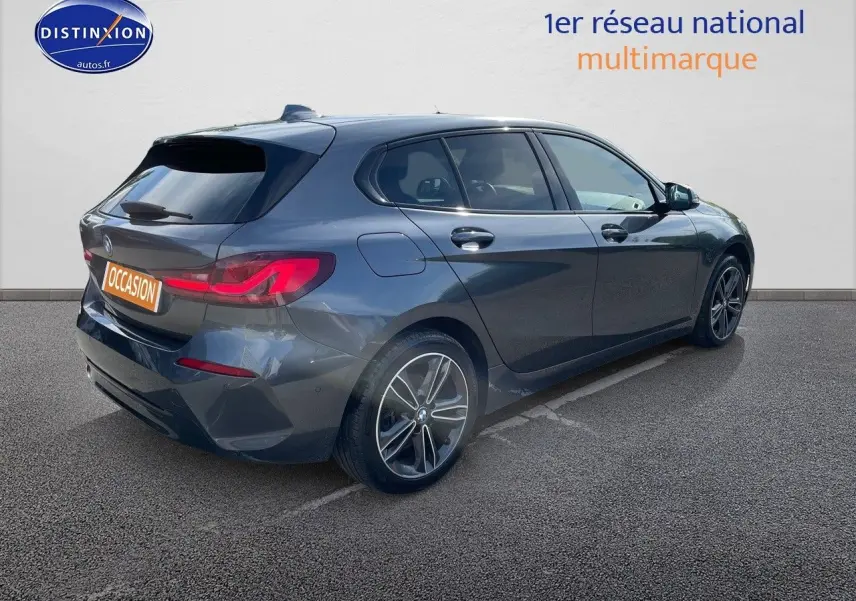 BMW Série 1 gris minéral métal vue 3/4 arrière côté gauche, avec feux arrière LED et jantes bi-ton.