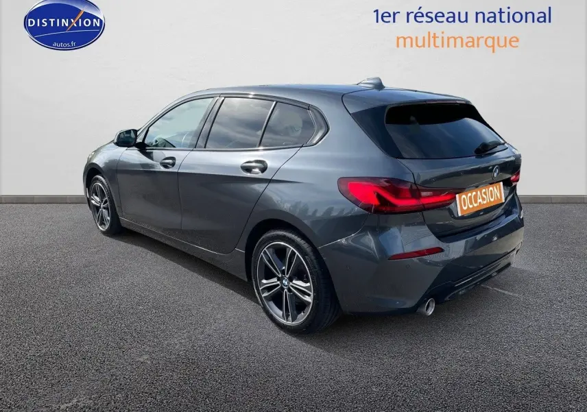 BMW Série 1 gris minéral métal vue 3/4 arrière côté gauche, avec feux arrière LED et jantes alliage bicolores.