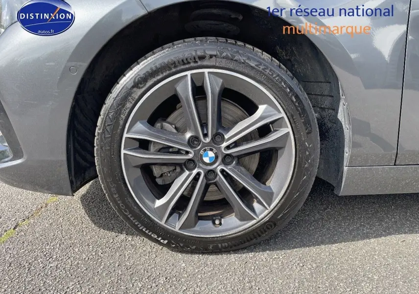 Gros plan sur la roue avant gauche gris minéral métal d'une BMW Série 1 118i Edition Sport avec jante alliage bi-ton.