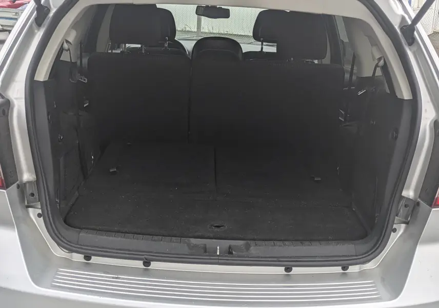 Vue 3/4 avant droit d'un FIAT Freemont gris avec barres de toit et jantes alu dans un showroom blanc.