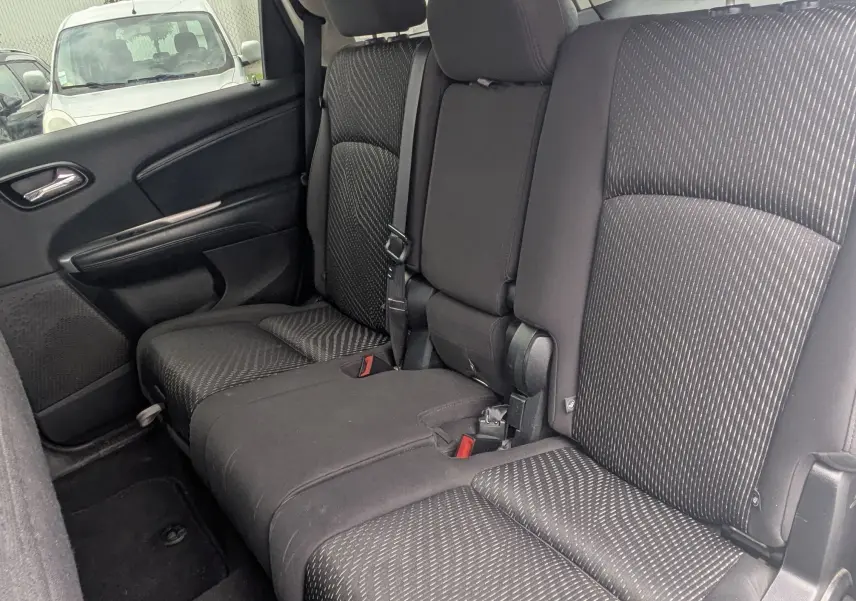 Vue de profil côté gauche d'un FIAT Freemont gris avec barres de toit et jantes alu dans un studio blanc.