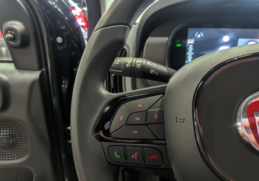 Gros plan sur le volant noir de la FIAT Panda 2025 hybride, montrant les commandes intégrées et le tableau de bord numérique.