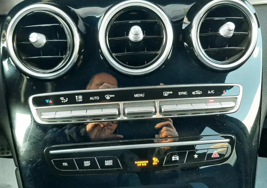 Vue rapprochée du tableau de bord noir brillant du Mercedes GLC Coupé 300 AMG Line, montrant les aérateurs ronds et commandes climatiques.