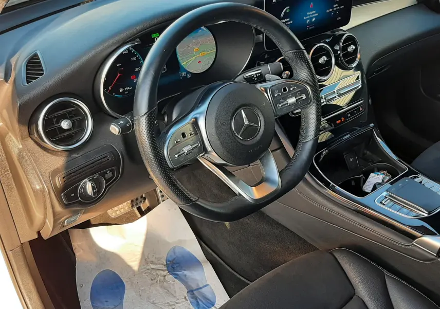 Vue intérieure côté conducteur du Mercedes GLC Coupé blanc 2019, tableau de bord moderne avec écran tactile et volant multifonction cuir.