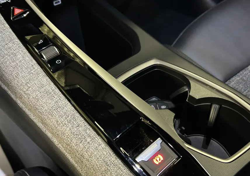 Gros plan sur la console centrale noire et grise du Peugeot 3008 III Hybrid 145 e-DSC6 Allure avec frein à main électrique activé.