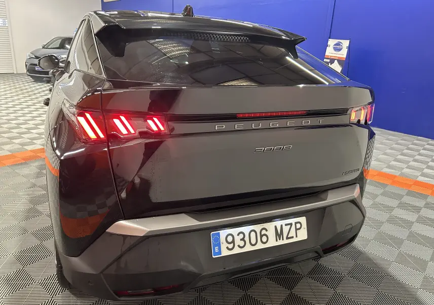 Vue 3/4 arrière d’un Peugeot 3008 noir hybride 2025 avec feux arrière LED distinctifs allumés dans un showroom.