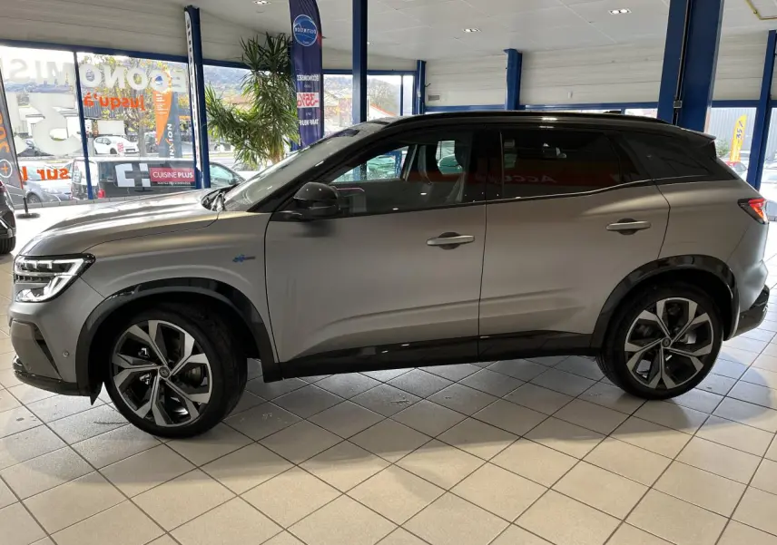 Vue latérale droite du Renault Austral gris avec toit noir étoilé et jantes alliage 20 pouces dans un showroom.