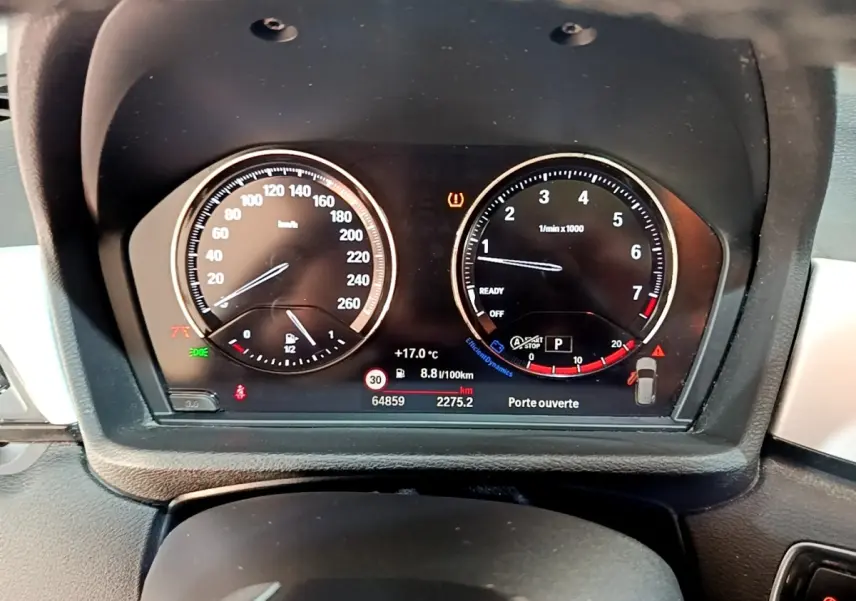 Vue rapprochée du tableau de bord numérique du BMW X1 noir, affichant vitesse, compte-tours et alertes.