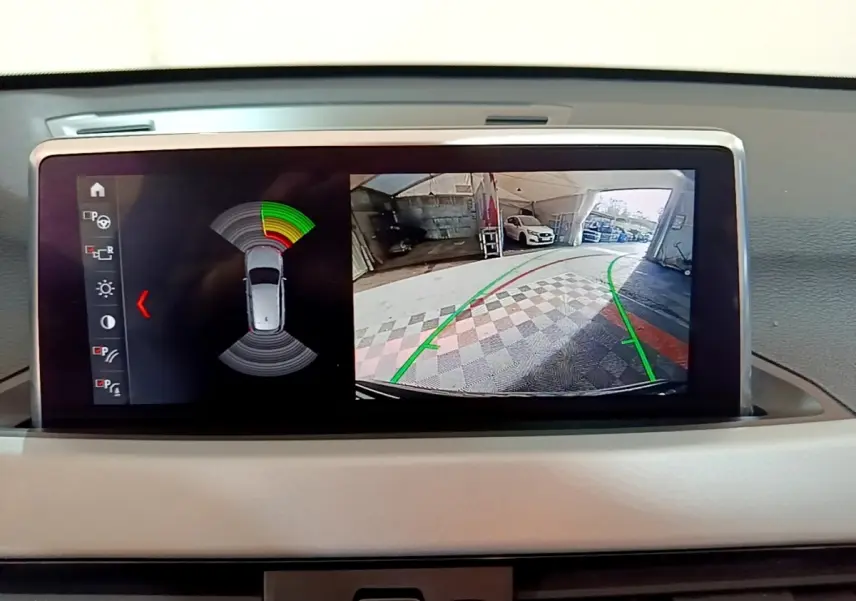 Écran tactile du système d’aide au stationnement de la BMW X1 noire, affichant la caméra de recul et les capteurs.