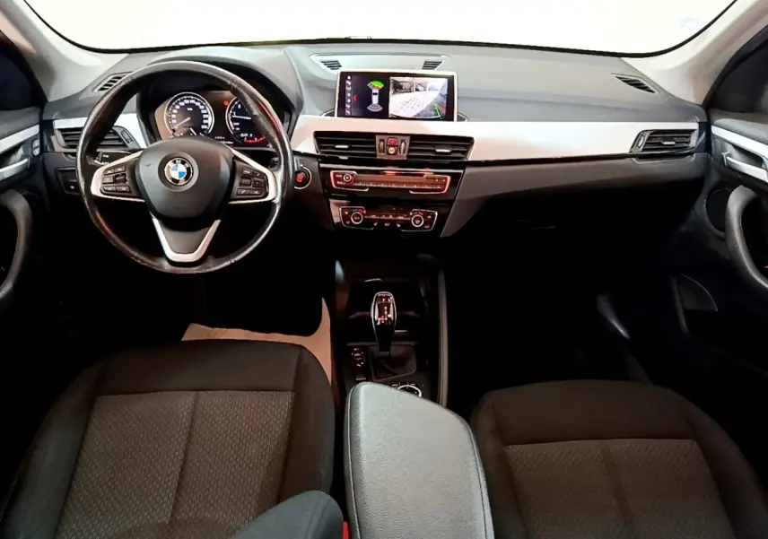 Vue intérieure avant du tableau de bord et volant cuir noir d'une BMW X1 sDrive20i avec écran tactile et boîte automatique.