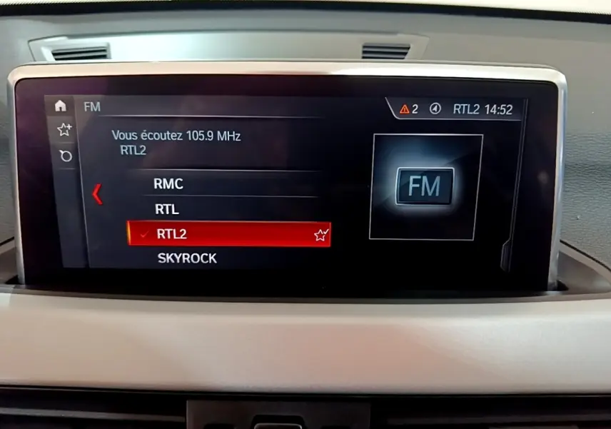 Écran tactile central du tableau de bord du BMW X1 noir, affichant les stations radio FM avec RTL2 sélectionnée.