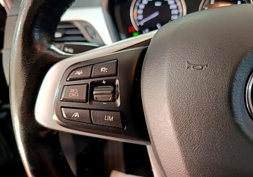 Gros plan sur le volant cuir noir de la BMW X1 2020, avec commandes du régulateur de vitesse sur le côté gauche.